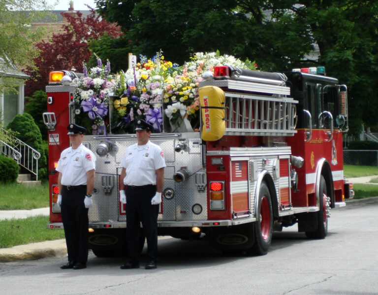 Fire engine with flowers on and two members walking behind